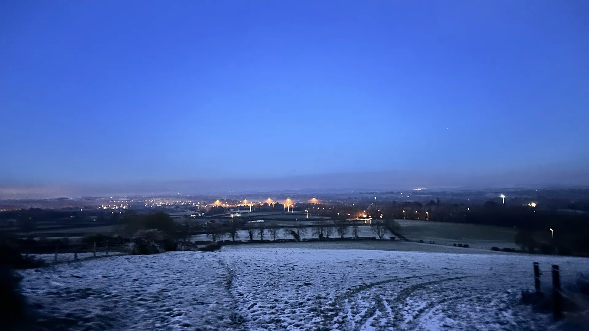 Snowy landscape overlooking a city skyline with illuminated buildings and bridges in the distance.